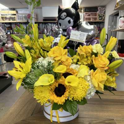 Yellow floral arrangement with lilies, roses, sunflowers, and calla lilies in a white box