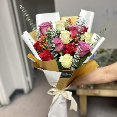 Bouquet of red, pink, and cream roses wrapped in white and gold paper