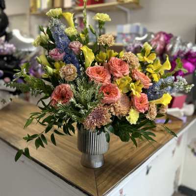Mixed bouquet in a ribbed silver vase with pink, yellow, and blue flowers