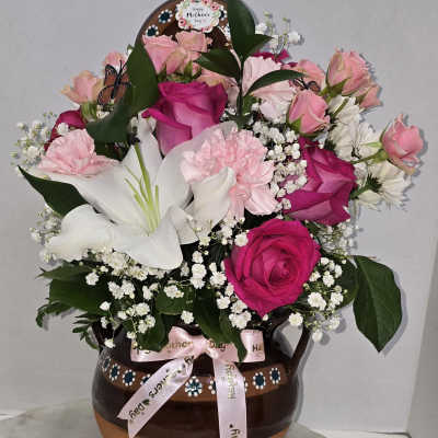 Pink and white flower arrangement in a brown ceramic vase with a ribbon
