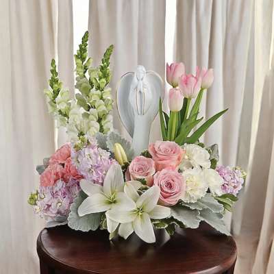 Pink tulips and roses arranged with white lilies and a figurine centerpiece