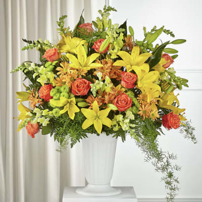Bright mixed bouquet in a white pedestal vase with yellow lilies and orange roses