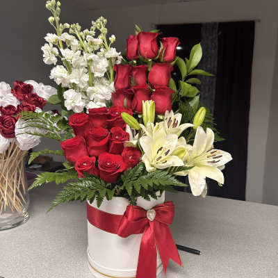Red roses and white lilies arranged in a white hat box with a red ribbon