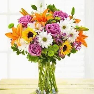 Mixed bouquet of orange lilies, pink roses, and white daisies in a glass vase