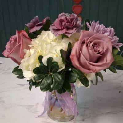 Pink and white flower arrangement in a glass jar with a lavender ribbon