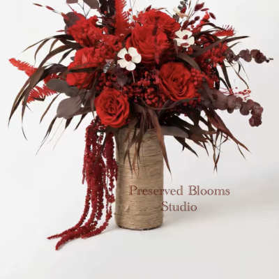 Tall arrangement of deep red roses and berries in a twine-wrapped cylinder vase