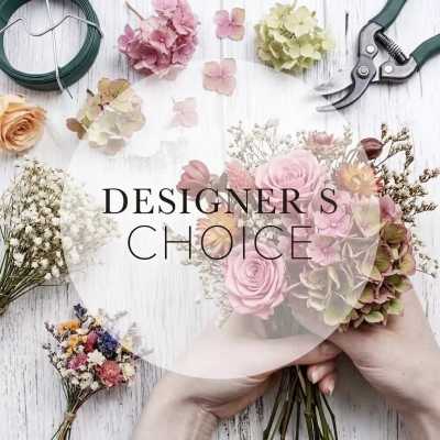 Hands holding a pastel mixed flower bouquet on a worktable with tools and loose blooms