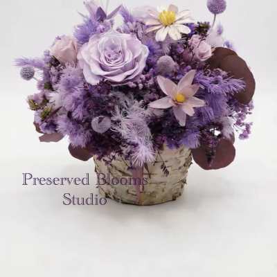 Lavender and purple flower arrangement with roses and daisies in a birch-wrapped pot