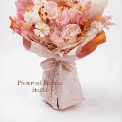 Pink and white bouquet of roses and daisy-like blooms wrapped in pink and orange paper with a bow.
