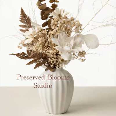 Neutral dried flower arrangement with white blooms and brown foliage in a white ceramic vase