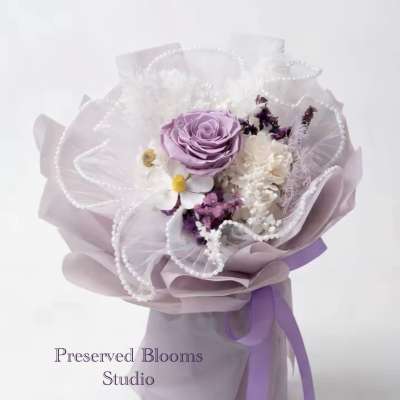 Hand-tied bouquet of lavender and white flowers wrapped in lilac paper with pearl accents and ribbon.