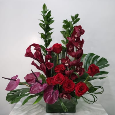 Red roses and burgundy orchids arranged in a glass vase