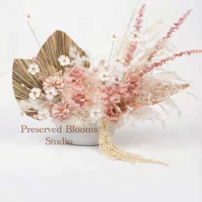 Low arrangement of blush roses, white daisy-like flowers, and dried accents in a white bowl.