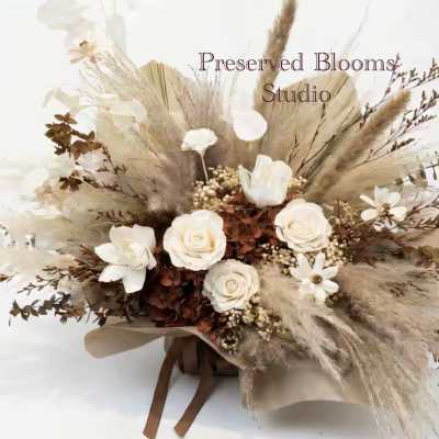 Neutral dried flower arrangement with white roses and beige grasses wrapped in brown paper with ribbons