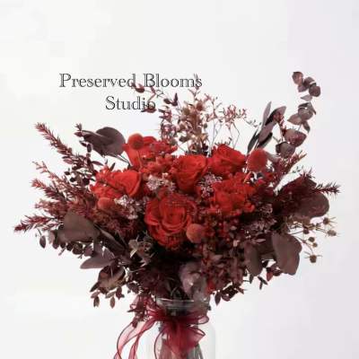 Tall bouquet of red roses and burgundy dried elements in a glass jar with red ribbon