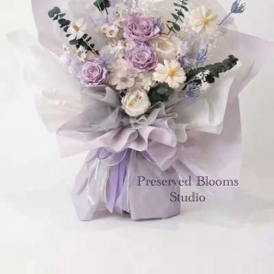Hand-tied bouquet of lavender roses and white daisies wrapped in layered lilac and white paper.