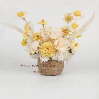 Yellow and cream preserved flower arrangement in a small woven basket container