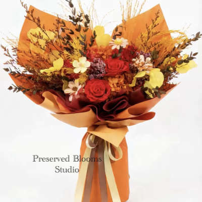 Tall bouquet of red and yellow flowers with dried accents wrapped in bright orange paper with ribbons
