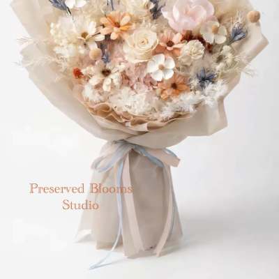 Pastel bouquet of preserved flowers wrapped in beige paper with blue and peach ribbon.