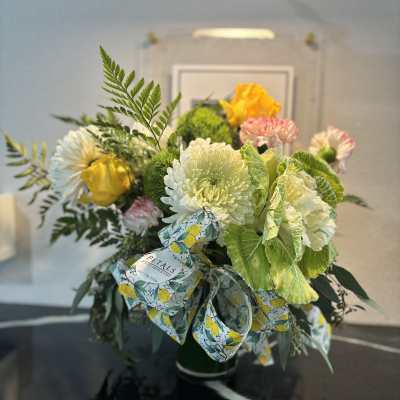 Bouquet of mixed flowers in a green vase with a patterned ribbon