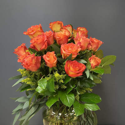 Orange roses arranged in a glass vase with greenery