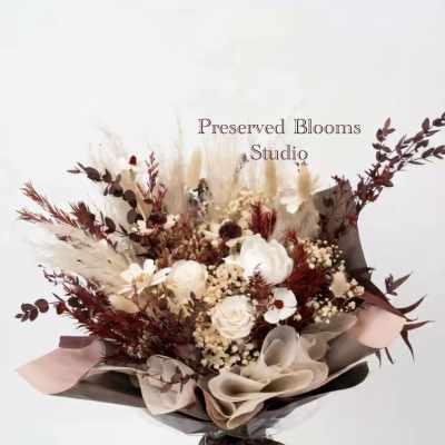 Bouquet of preserved white roses with burgundy dried foliage wrapped in brown and blush paper with a printed ribbon