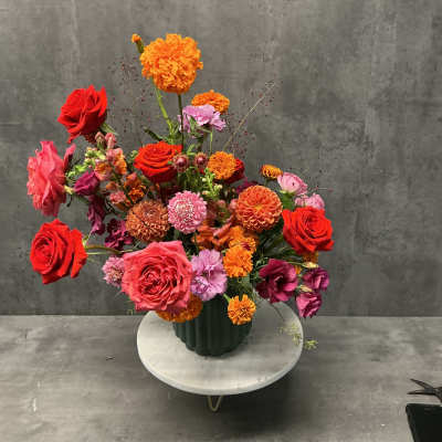 Mixed bouquet of red, pink, and orange flowers in a dark vase