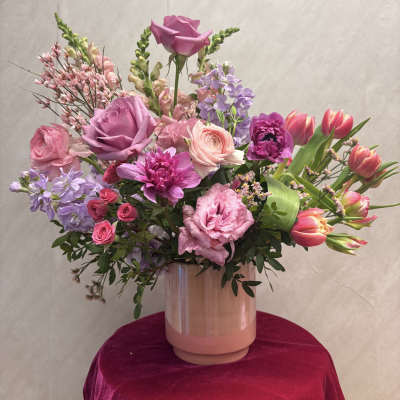 Tall arrangement of pink and purple roses, tulips, and mixed flowers in a peach ceramic vase