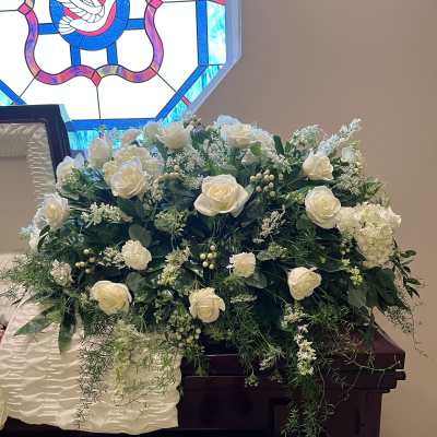 White rose arrangement on a dark wooden casket with trailing greenery