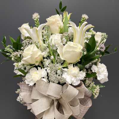 White roses and lilies in a glass vase with a large beige bow