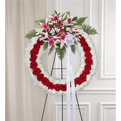Standing wreath of red roses and white flowers topped with pink and white lilies and a white ribbon
