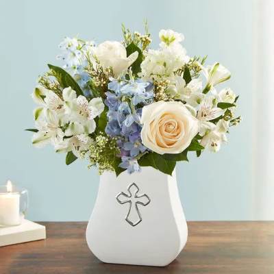 White and cream roses with blue and white blooms in a white vase with a cross emblem