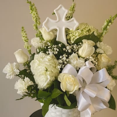 White floral arrangement in a basket with a cross topper and satin bow