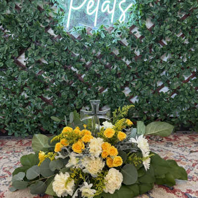 Yellow and white floral arrangement with a clear cross in front of a green wall