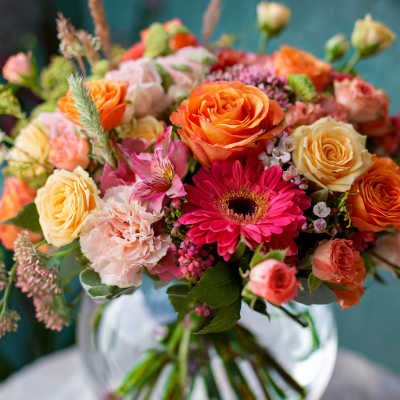 Mixed bouquet of orange, pink, and cream flowers in a glass vase