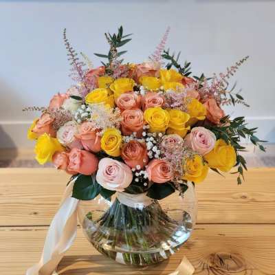 Bouquet of yellow and peach roses in a round glass vase