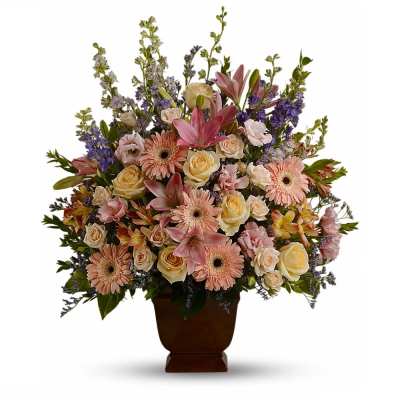 Tall arrangement of pastel roses, gerbera daisies, lilies and mixed blooms in a brown pedestal vase