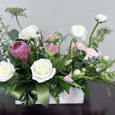 White and pink floral arrangement in a white box with a green ribbon