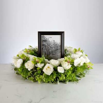 Round white and green floral wreath encircling a black-framed photograph.