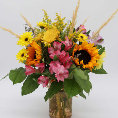 Bouquet of sunflowers, pink alstroemeria, and yellow daisies in a glass vase