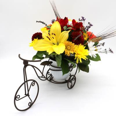 Mixed bouquet with a large yellow lily in a white vase on a decorative tricycle stand