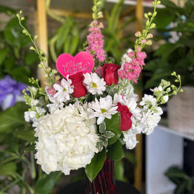 Bouquet of red roses, white daisies, and white hydrangea in a glass vase