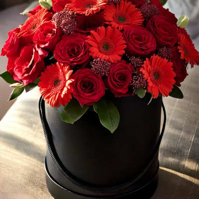 Red roses and gerbera daisies arranged in a black hatbox