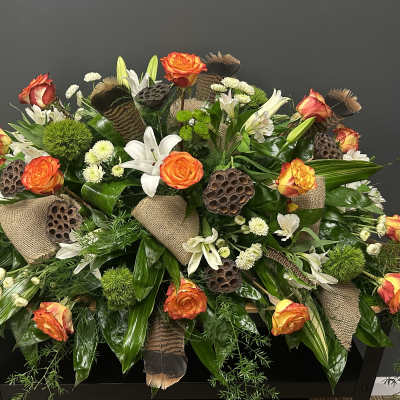 Large floral spray with orange roses, white lilies, and burlap accents