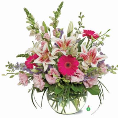 Low round arrangement of pink lilies and gerbera daisies in a clear glass bowl vase