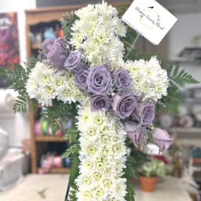 Standing white floral cross with lavender roses on an easel and a sympathy card at the top