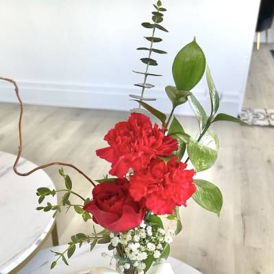 Red rose and carnations in a clear vase with a white ribbon