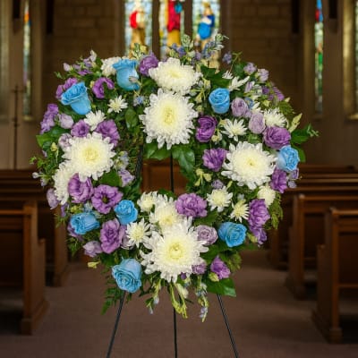Heart-shaped floral wreath on a stand with white, purple, and blue flowers