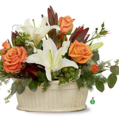Low arrangement of orange roses and white lilies in an ivory oval ceramic container