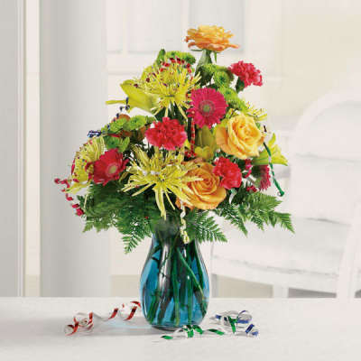 Bright mixed bouquet of yellow, orange, and red flowers in a blue glass vase with curling ribbons.